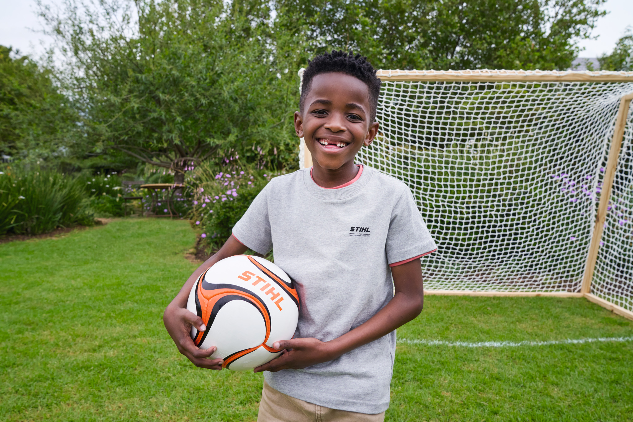 Ein Junge hält strahlend einen STIHL Fußball vor dem neuen Tor in der Hand