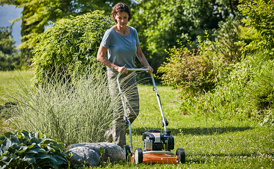 Frau mäht Rasen in ihrem Garten im Sommer mit STIHL Mulchrasenmäher RM 2 R