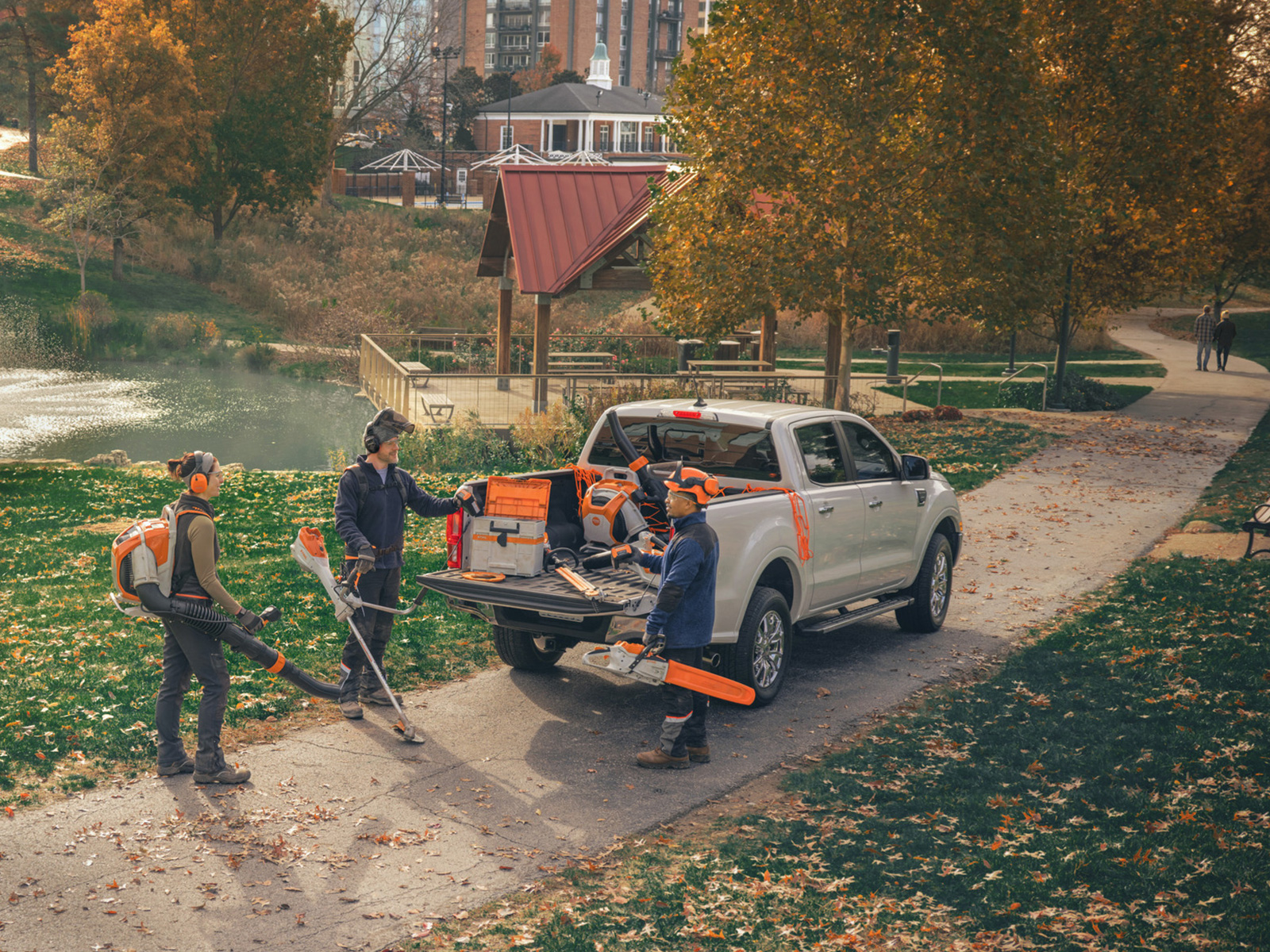 In einer Grünanlage arbeiten mehrere Personen mit STIHL Gartengeräten. Sie sind mit Freischneidern, Rasenmähern und Schutzausrüstung ausgestattet.