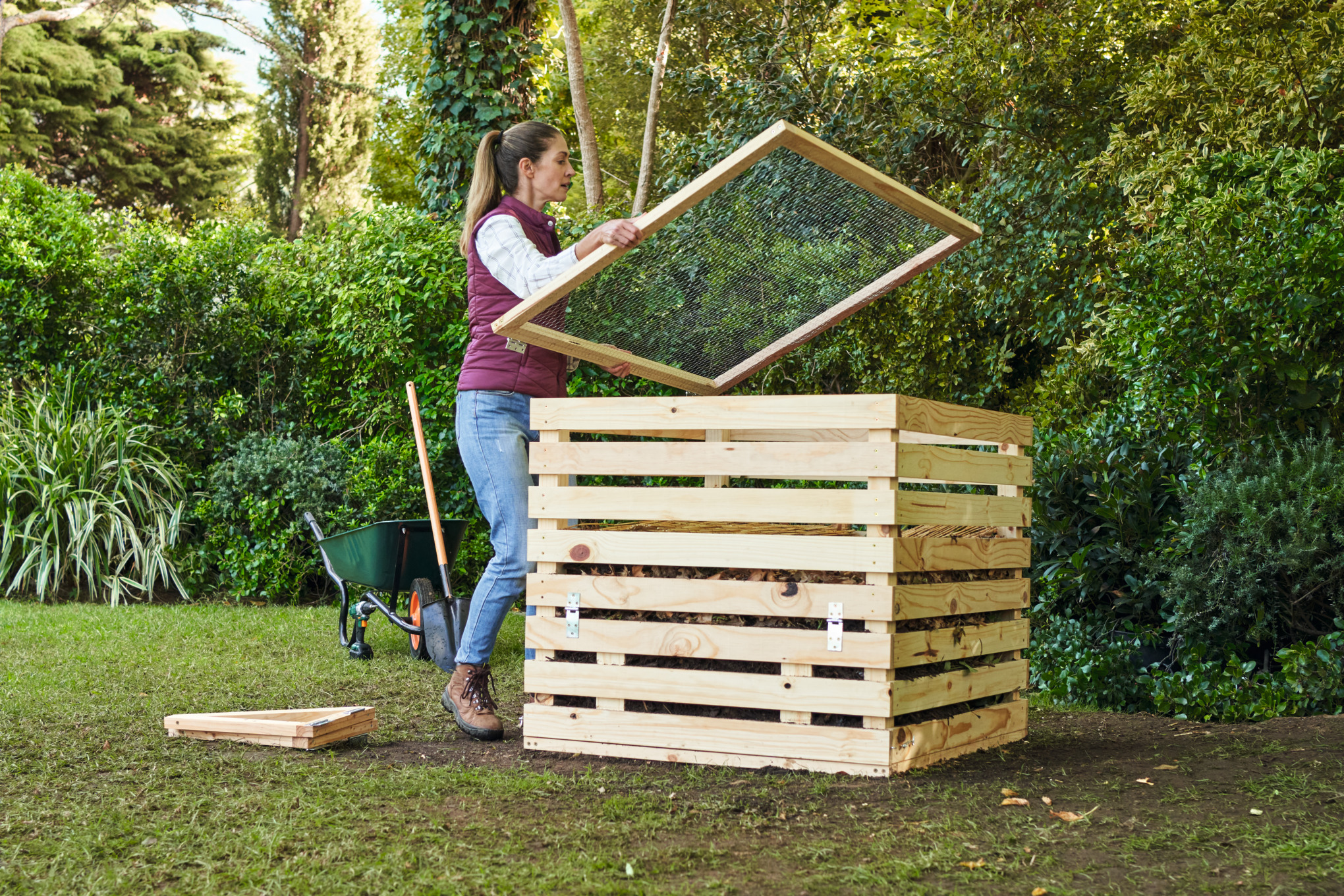 Frau auf einem Gartengrundstück deckt einen selber gebauten Komposter ab