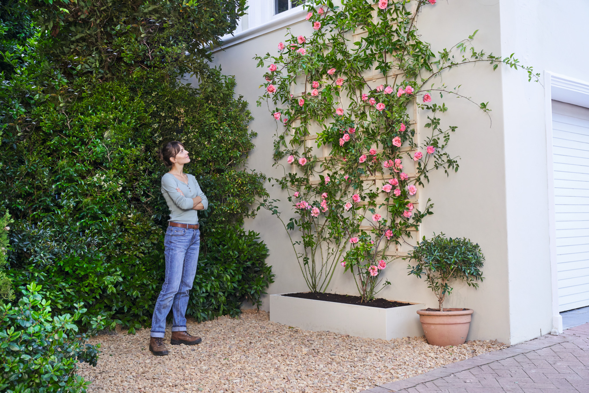 Eine Frau steht vor einer mit Rosenstrauch begrünten Fassade