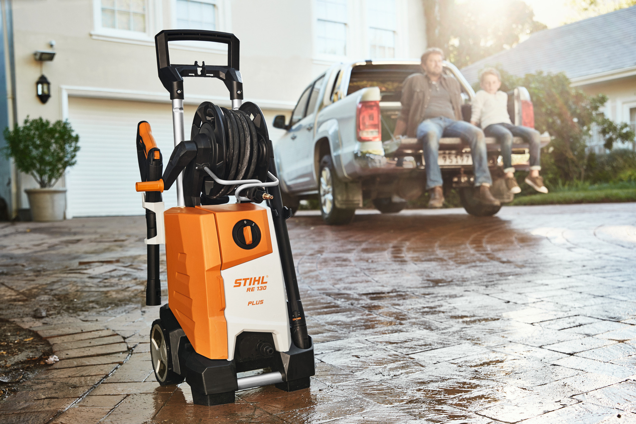  Eine Frau verlässt mit dem Hochdruckreiniger STIHL RE 130 PLUS eine Garage, um ihn zu benutzen 