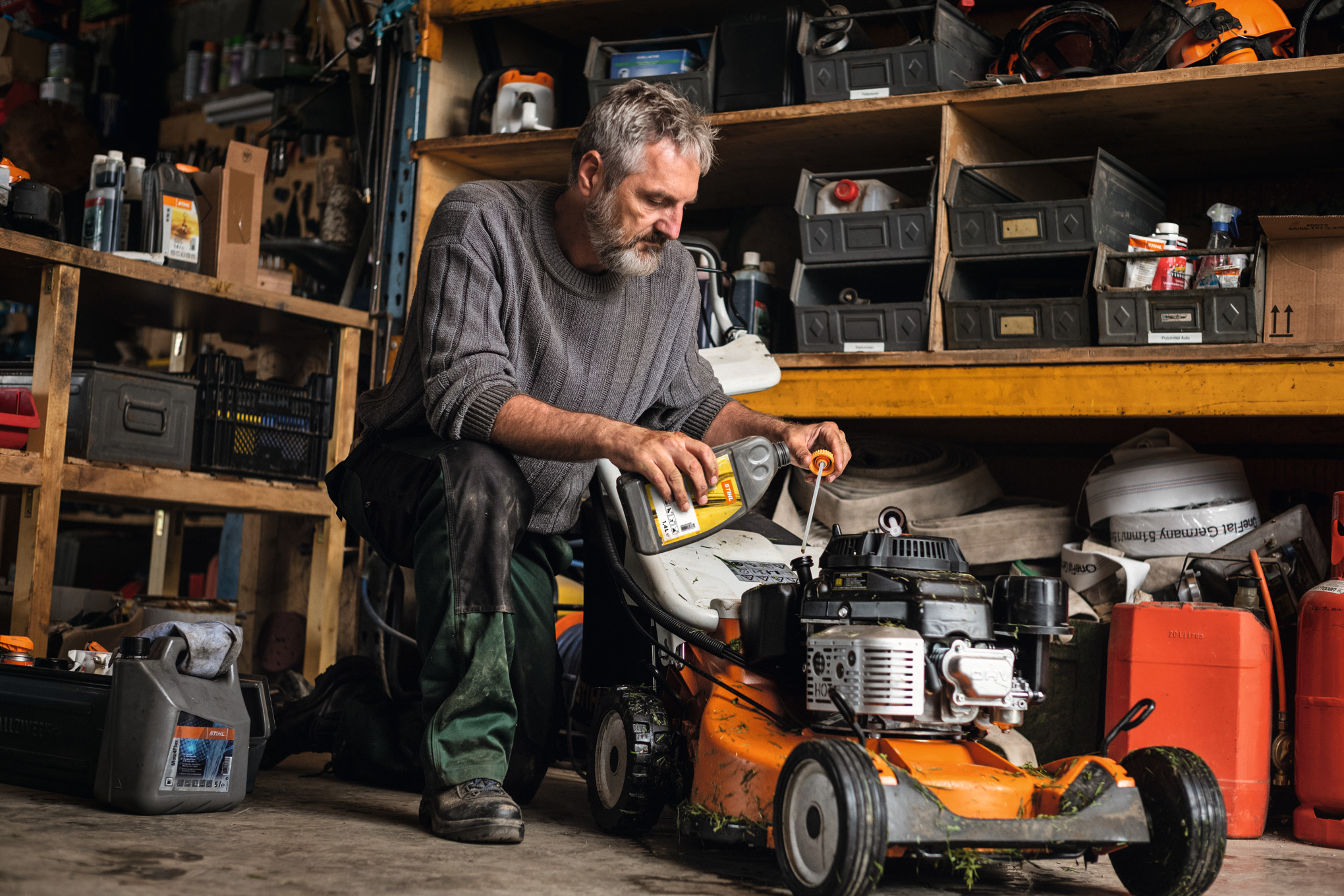 Mann wartet seinen Benzin-Rasenmäher STIHL RM 756 in der Garage