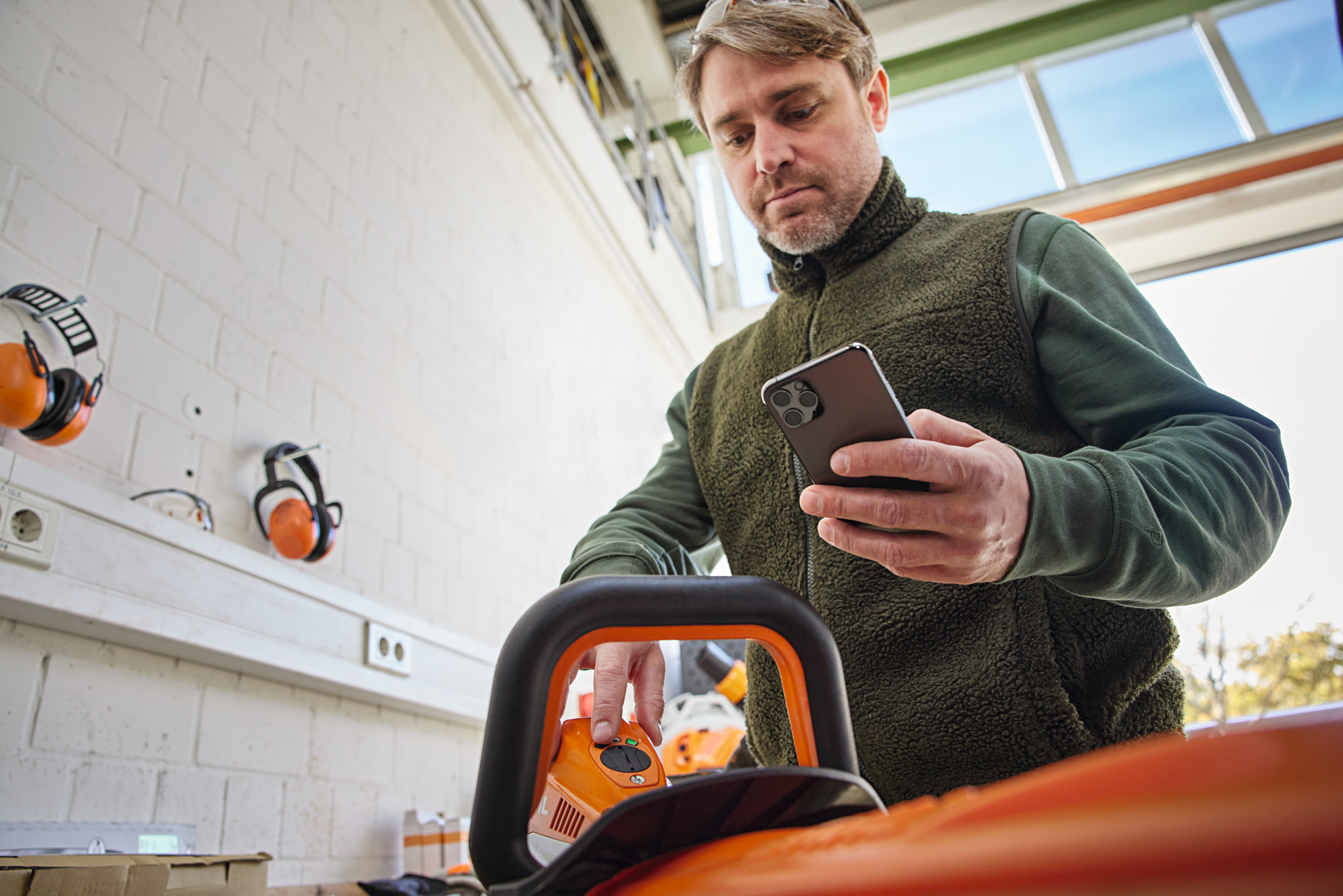 Person prüft den Maschinenstatus am Smart Connector 2 A und schaut mit der STIHL connected App auf ihr Smartphone