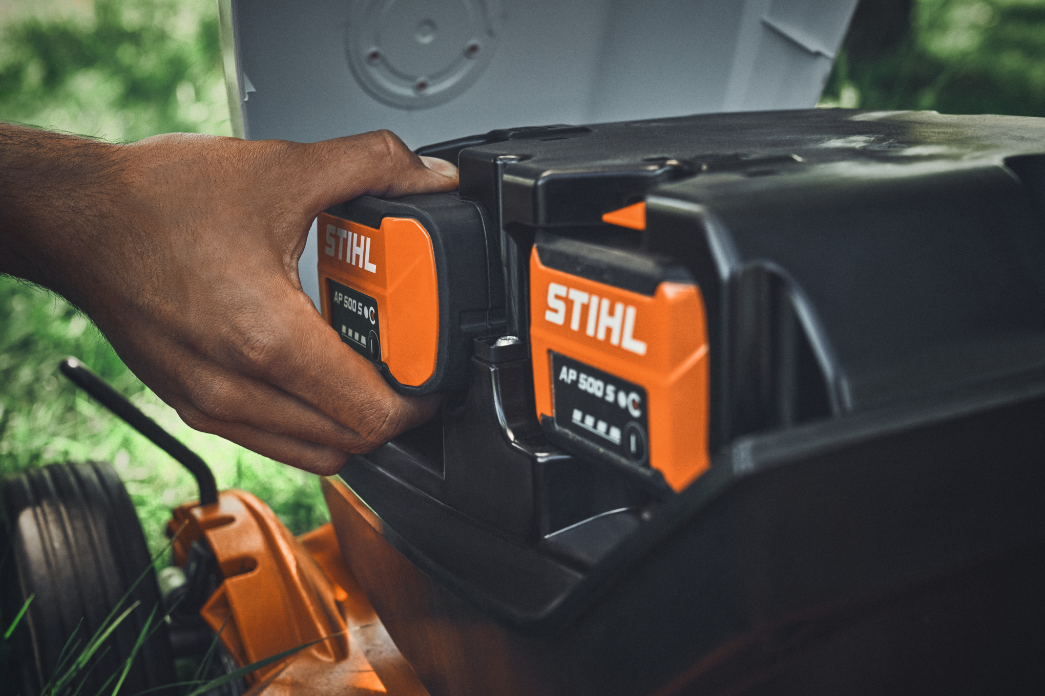 Eine Person steckt einen Akku STIHL AP 500 S in einen STIHL Akku-Rasenmäher