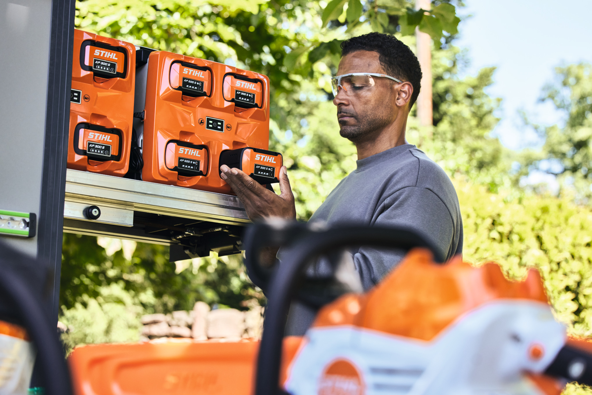 Ein Mann mit Schutzbrille entnimmt dem bottTainer einen STIHL Akku AP 300 S