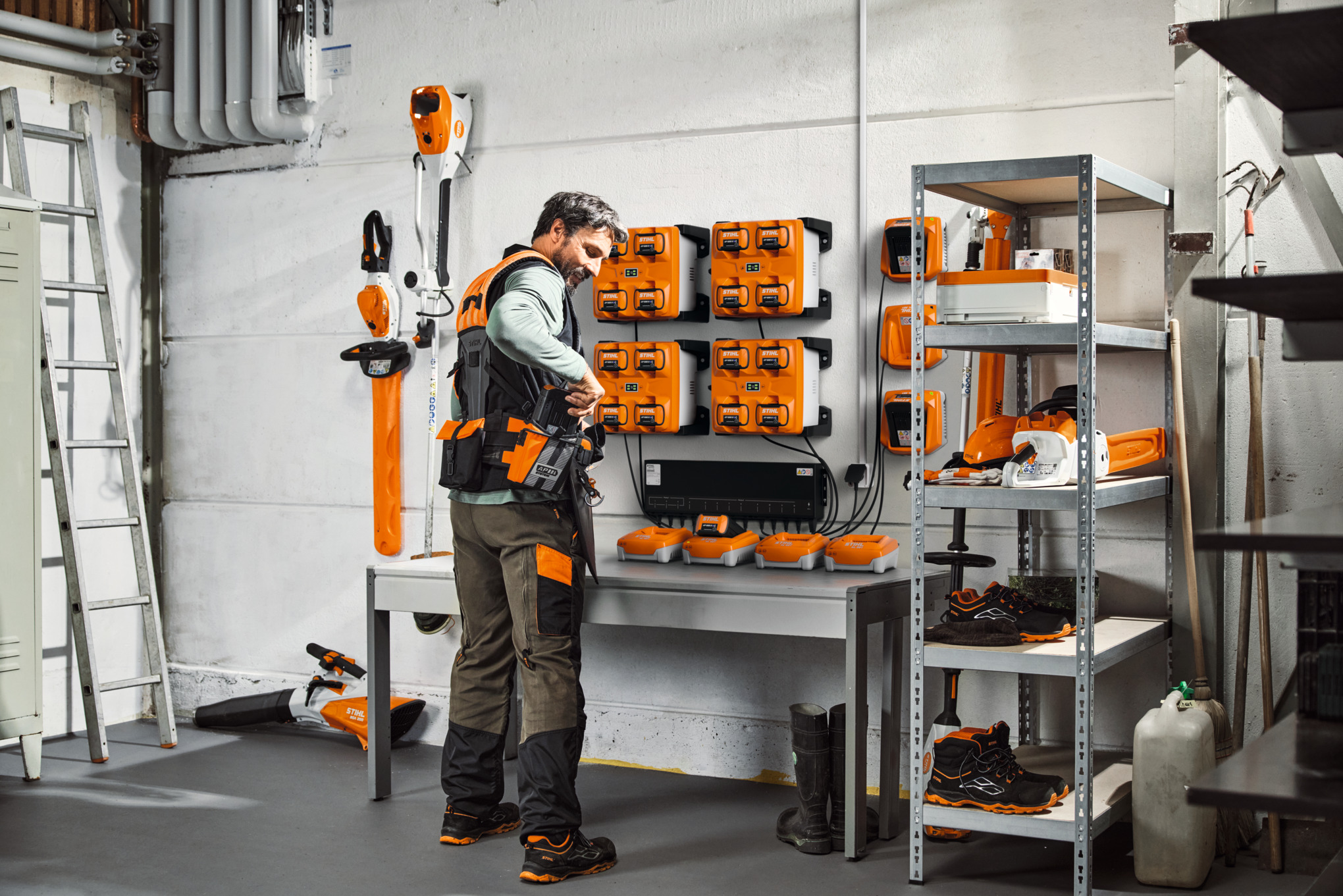 Ein Mann in einem Lagerraum mit STIHL Geräten und Akkus trägt das modulare Gurtsystem STIHL ADVANCE X-Flex 