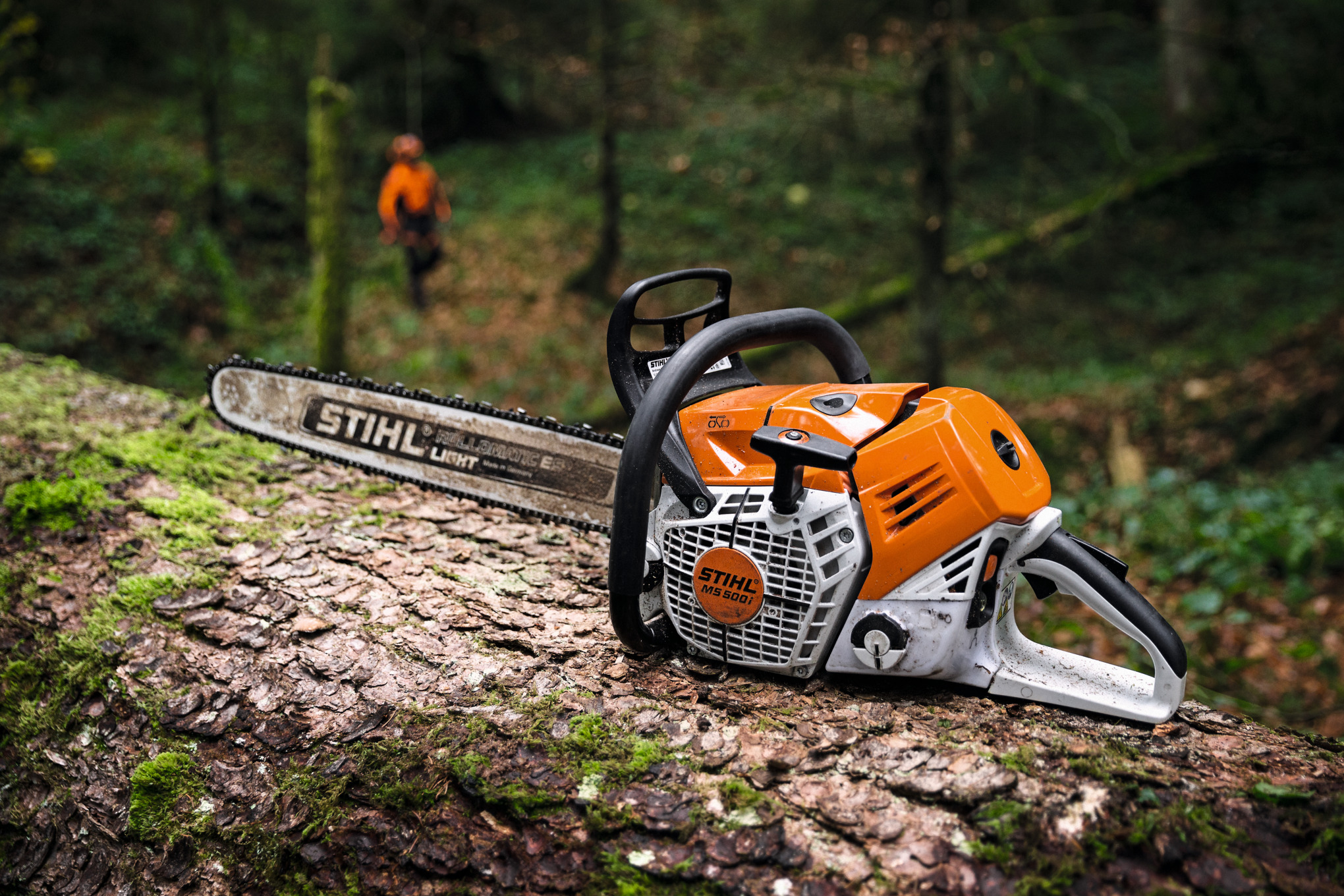 STIHL Motorsäge MS 500i Nahaufnahme auf einem Baumstamm liegend und Förster im Hintergrund