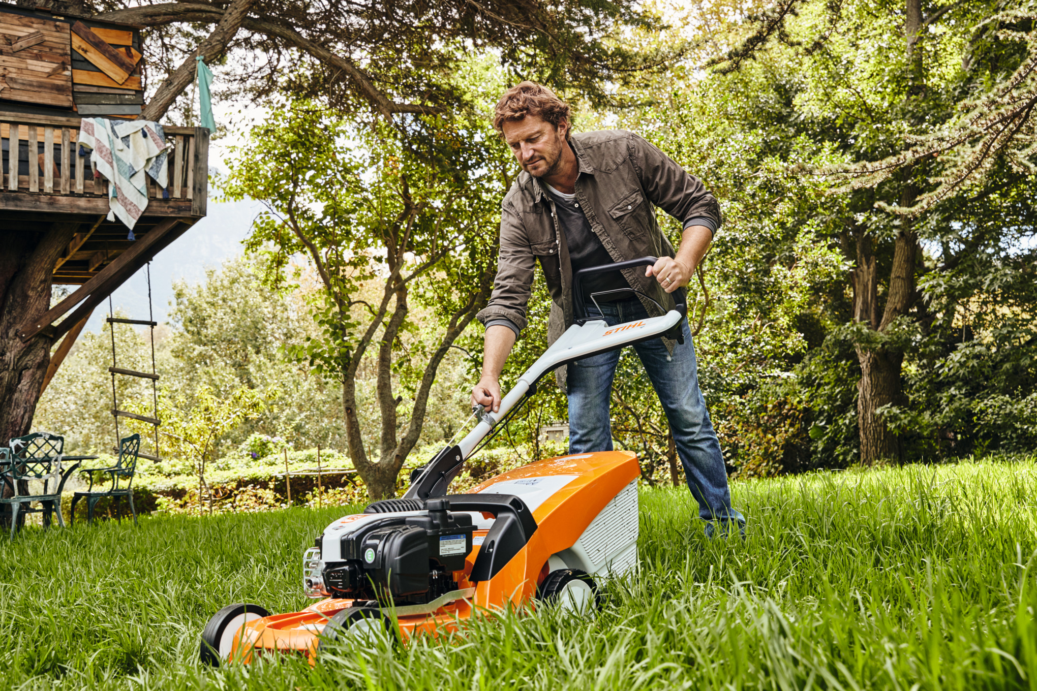 Ein Mann mäht mit einem Benzin-Rasenmäher STIHL RM 448 TC eine Gartenwiese