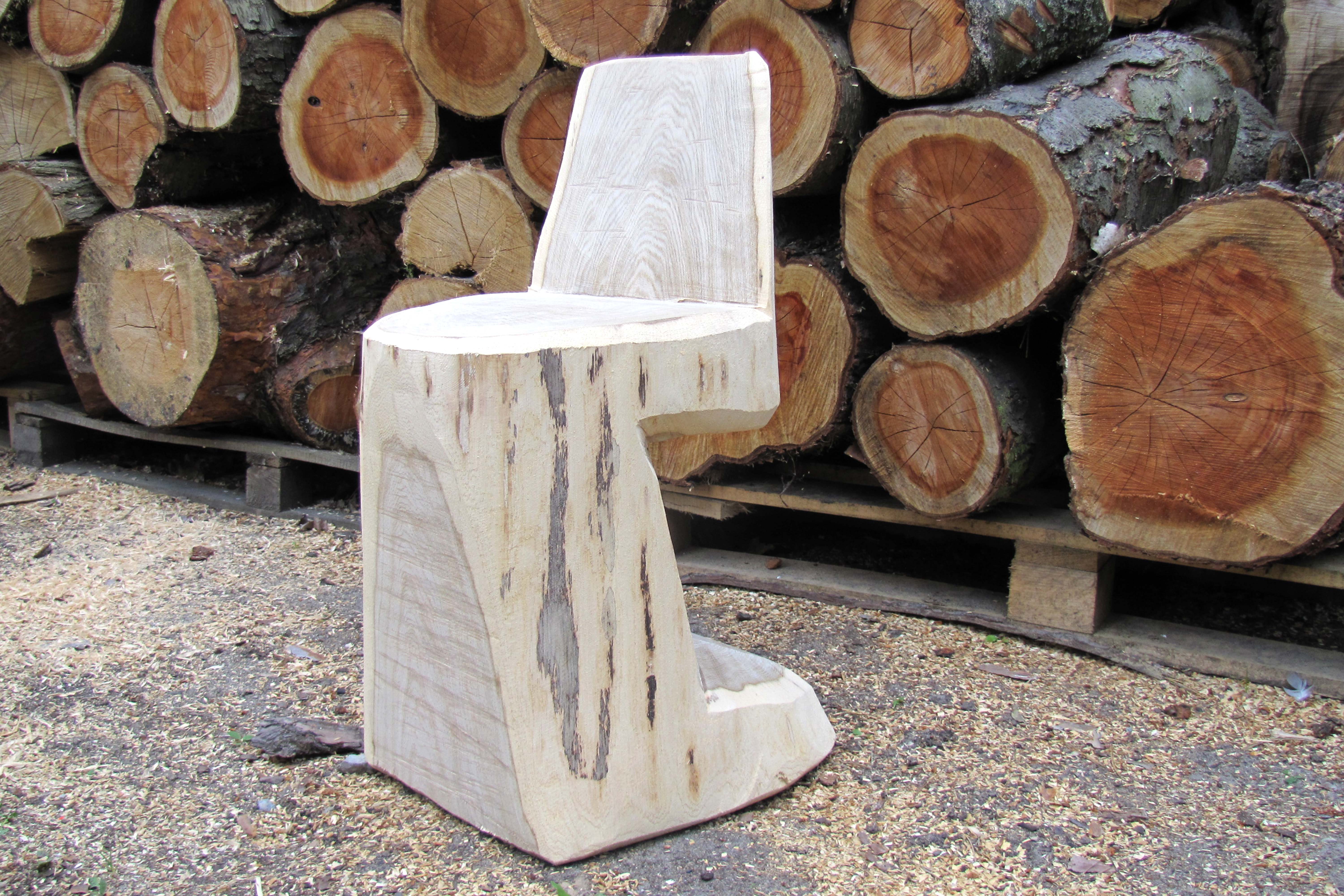 Holzstuhl zum Selberbauen vor einem Stapel mit Baumstämmen