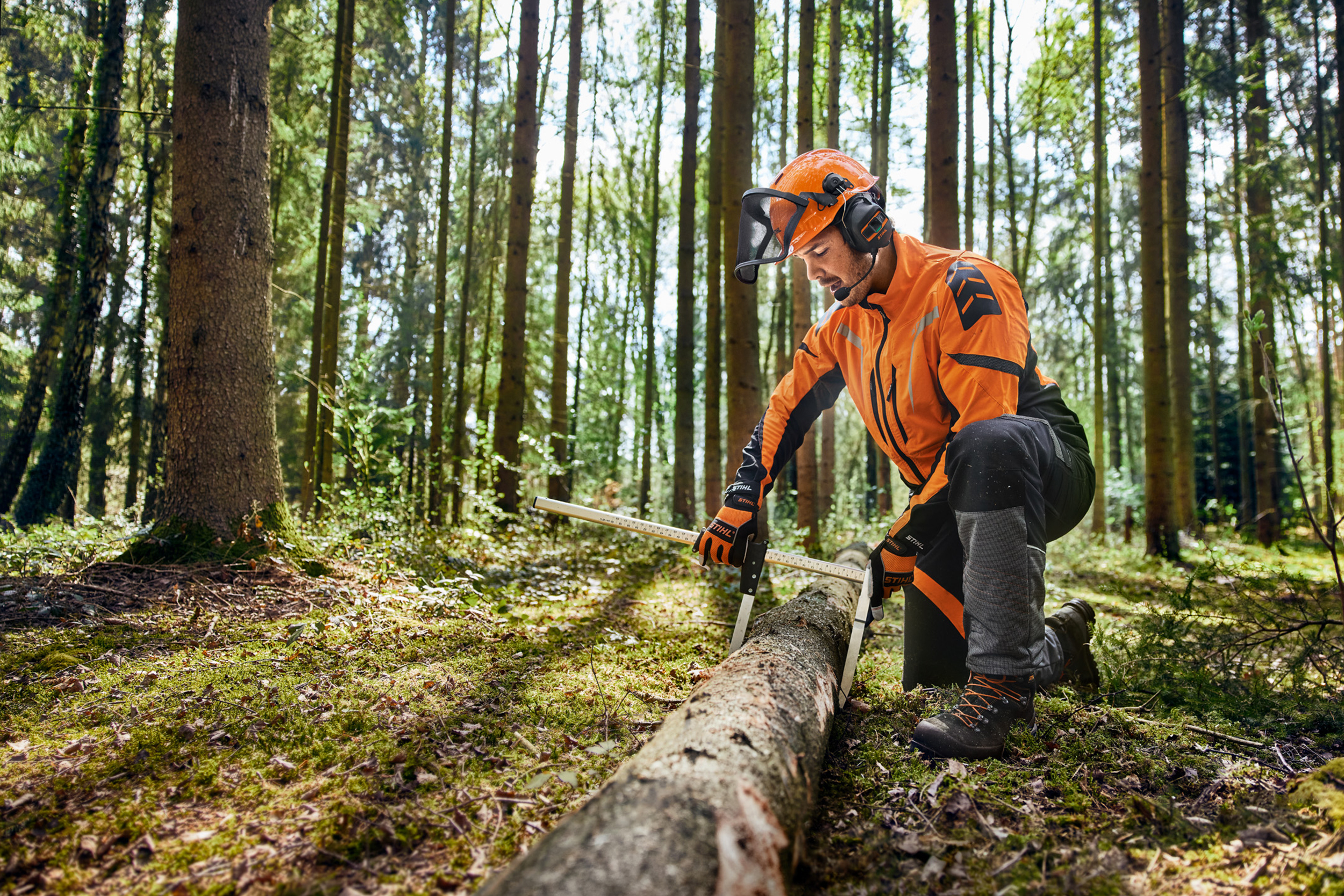 Forstarbeiter mit ProCOM Gehörschutz misst einen Baumstamm im Wald.