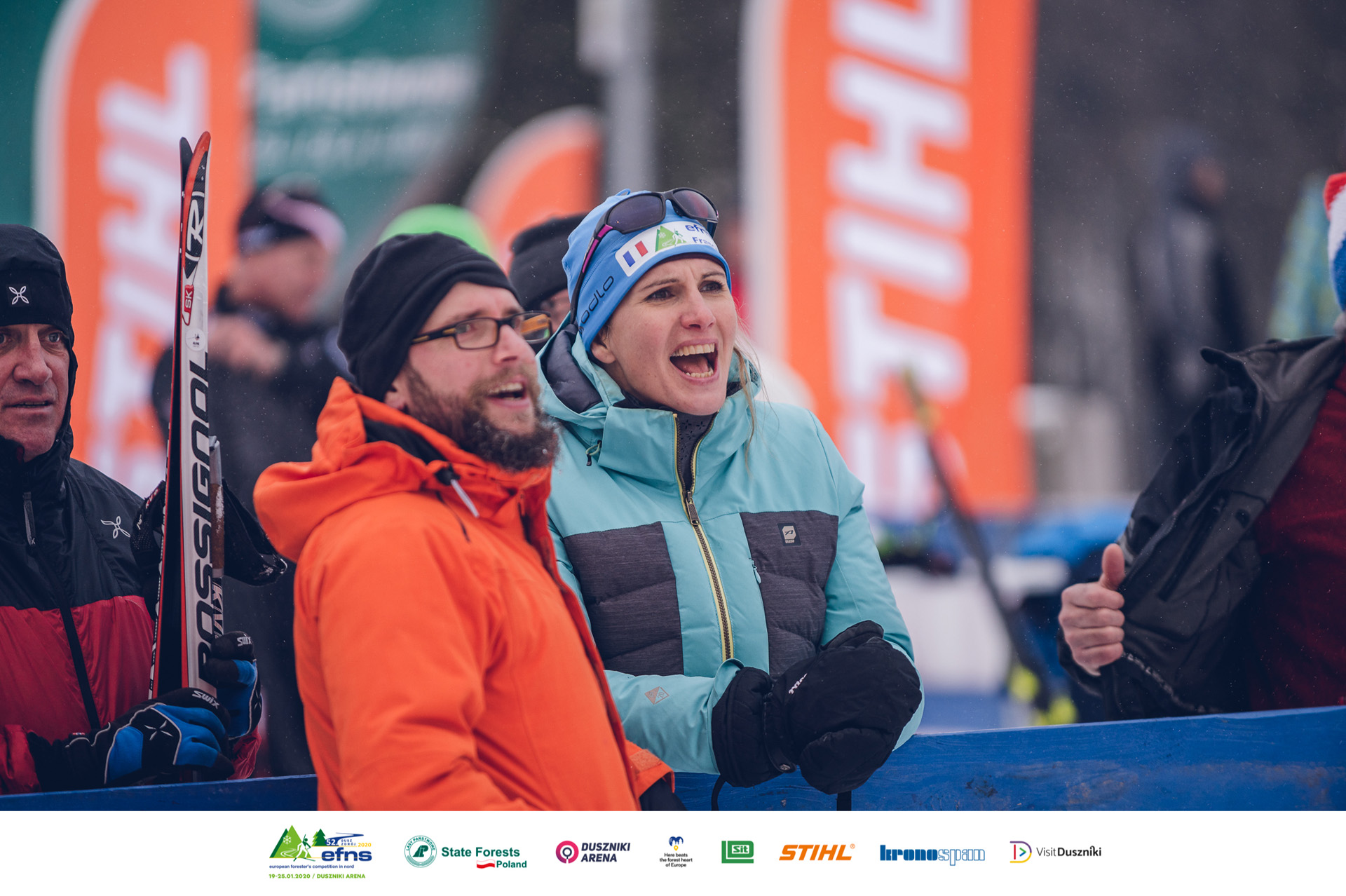 Mann und Frau jubeln bei der Nordischen Ski EM der Förster (EFNS) mit STIHL Flaggen im Hintergrund