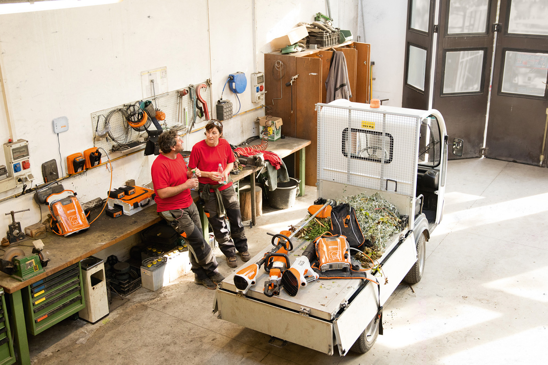 Zwei Personen machen in einer Werkstatt Pause neben kleinem Lastwagen mit STIHL Geräten auf der Ladefläche