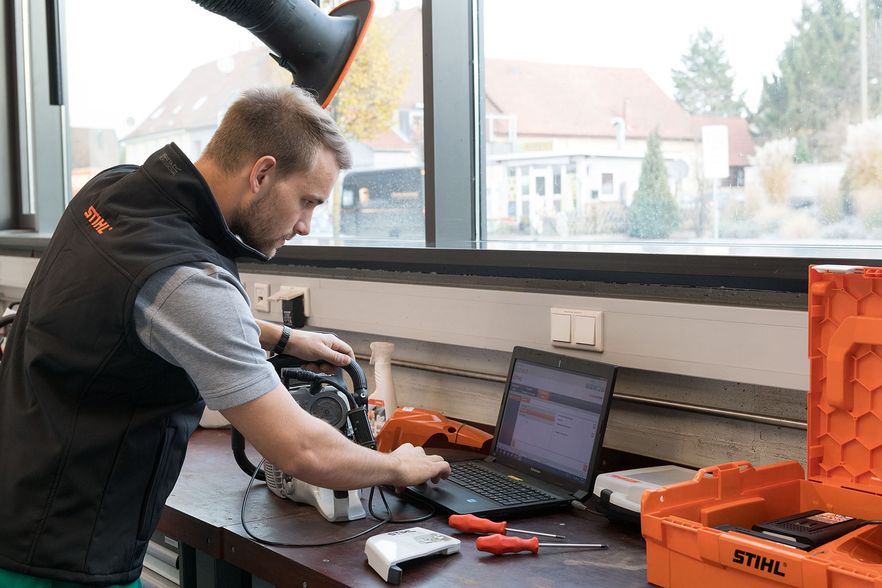 Mann schaut in einer Werkstatt auf einen Laptop. Daneben eine STIHL Kettensäge.