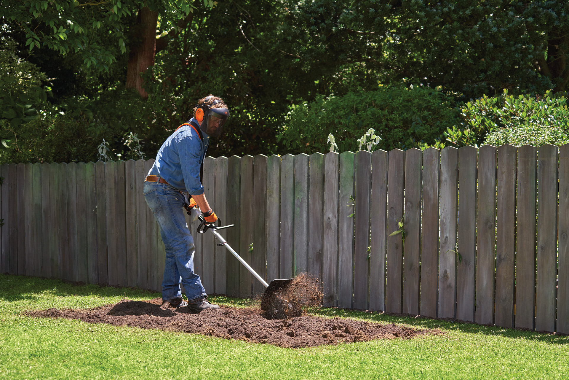 Person in Schutzausrüstung gräbt eine Fläche im Garten für ein Gemüsebeet mit einem STIHL KombiSystem mit Bodenfräse um