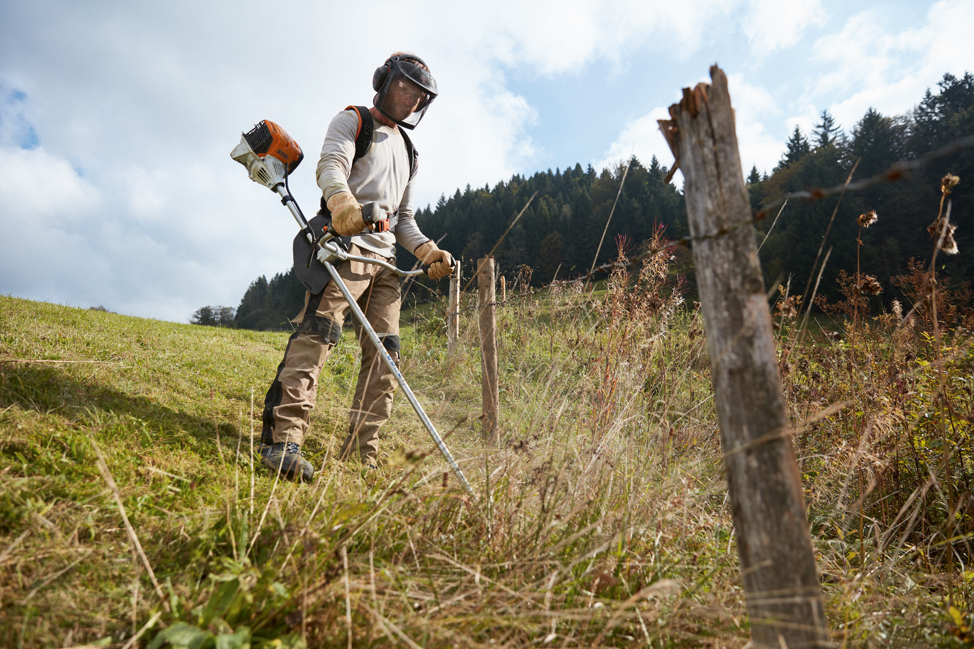 Mann in Schutzausrüstung mäht Rasen am Hang mit einem STIHL Benzin-Freischneider FS 91