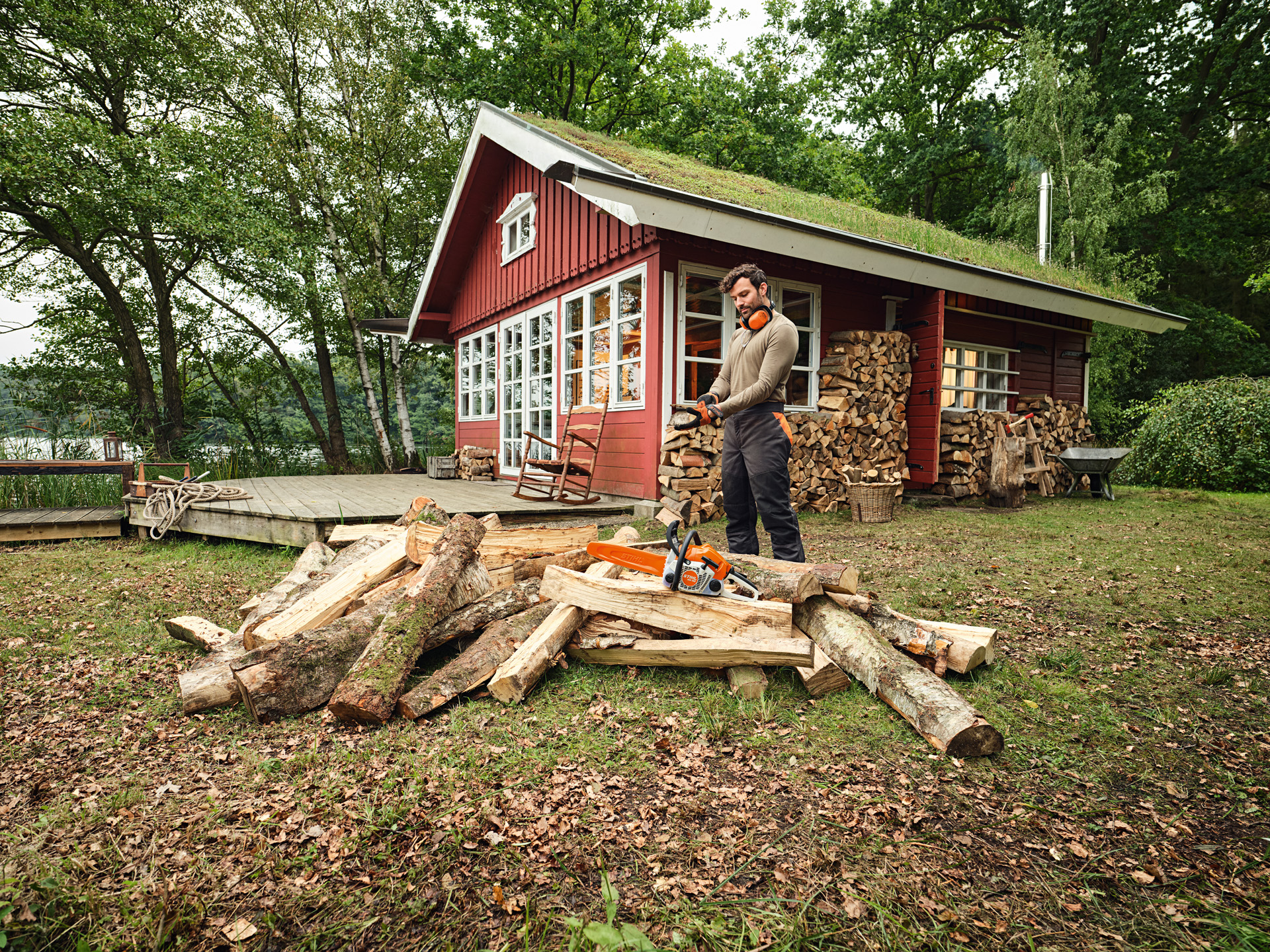 Ein Mann steht vor einem Holzstapel im Wald auf dem die STIHl MS 162 liegt. 