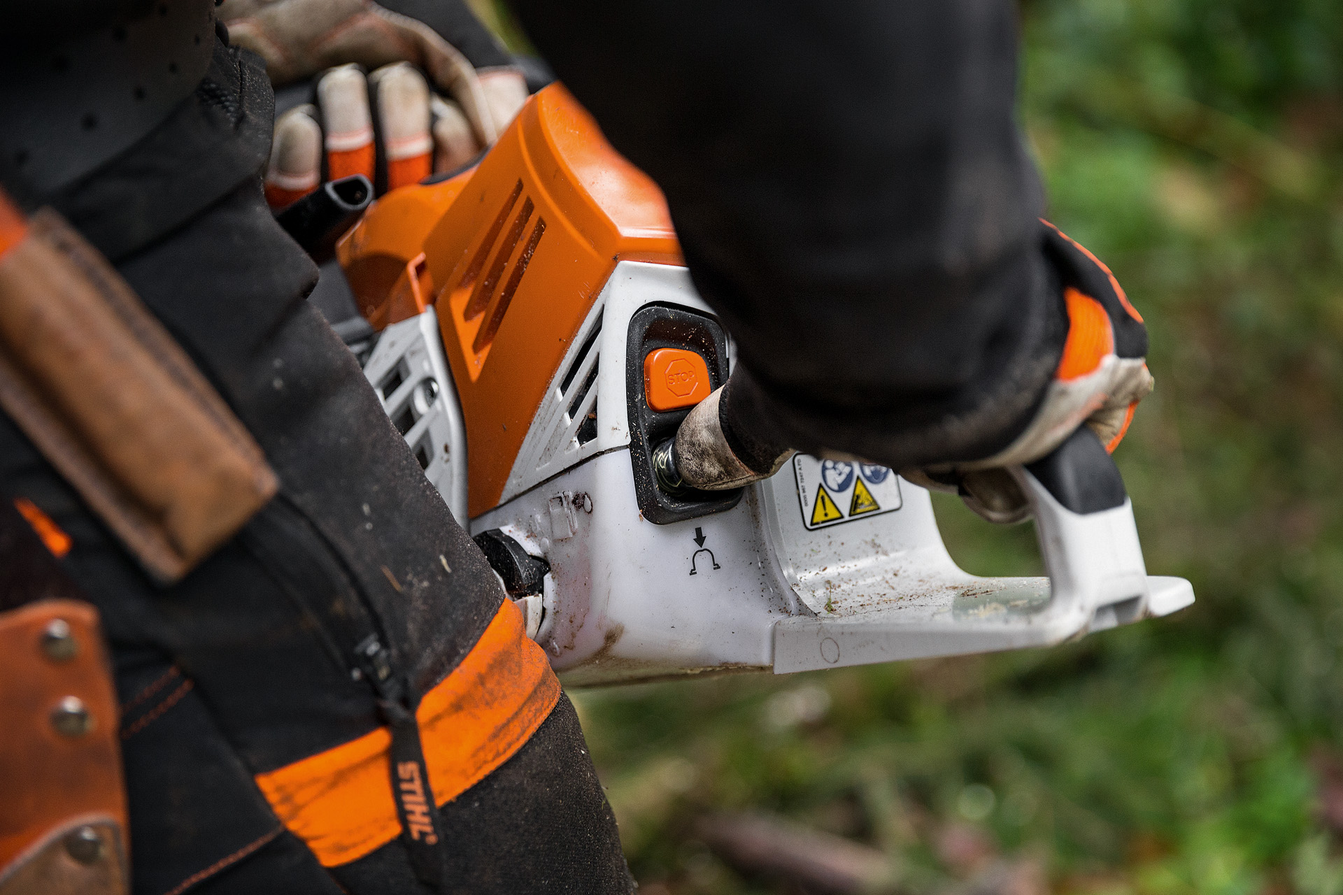 Person in Schutzkleidung startet STIHL Benzin-Kettensäge MS 500i im Laubwald auf dem Boden