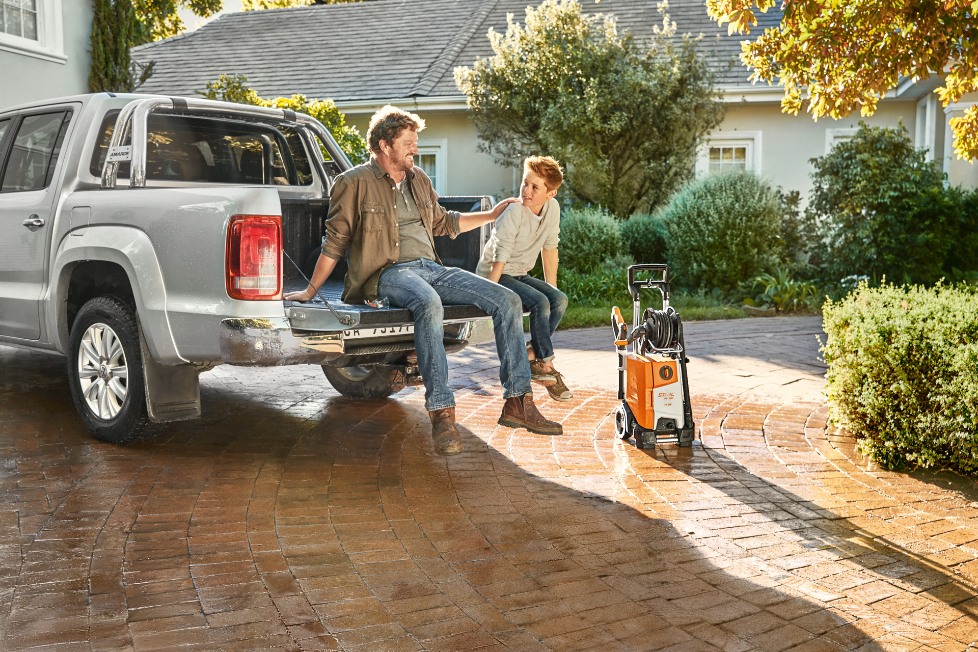 Vater und Sohn sitzen auf Ladefläche eines Pickups und neben dem Fahrzeug steht ein STIHL Hochdruckreiniger RE 130 plus