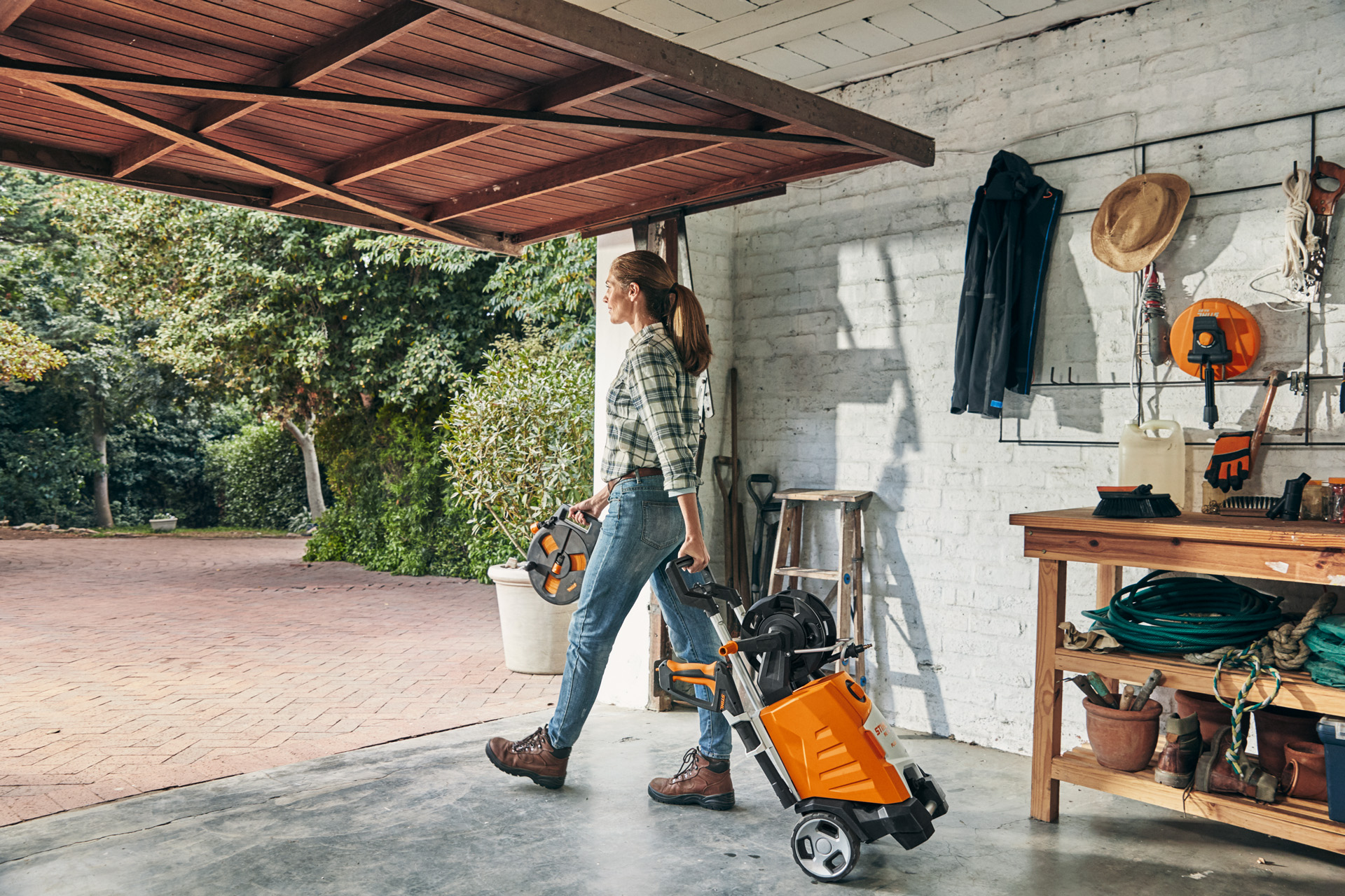 Eine Frau verlässt mit dem Hochdruckreiniger STIHL RE 130 PLUS eine Garage, um ihn zu benutzen