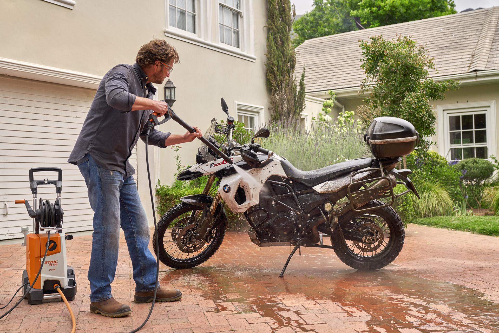 Mann reinigt sein Motorrad vor dem Haus mit einem STIHL Hochdruckreiniger RE 130 plus