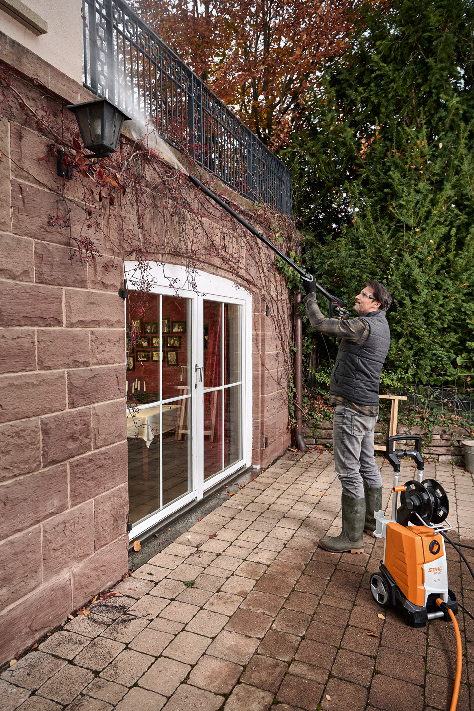 Mann steht auf Terrasse und reinigt die Fassade mit einem STIHL Hochdruckreiniger