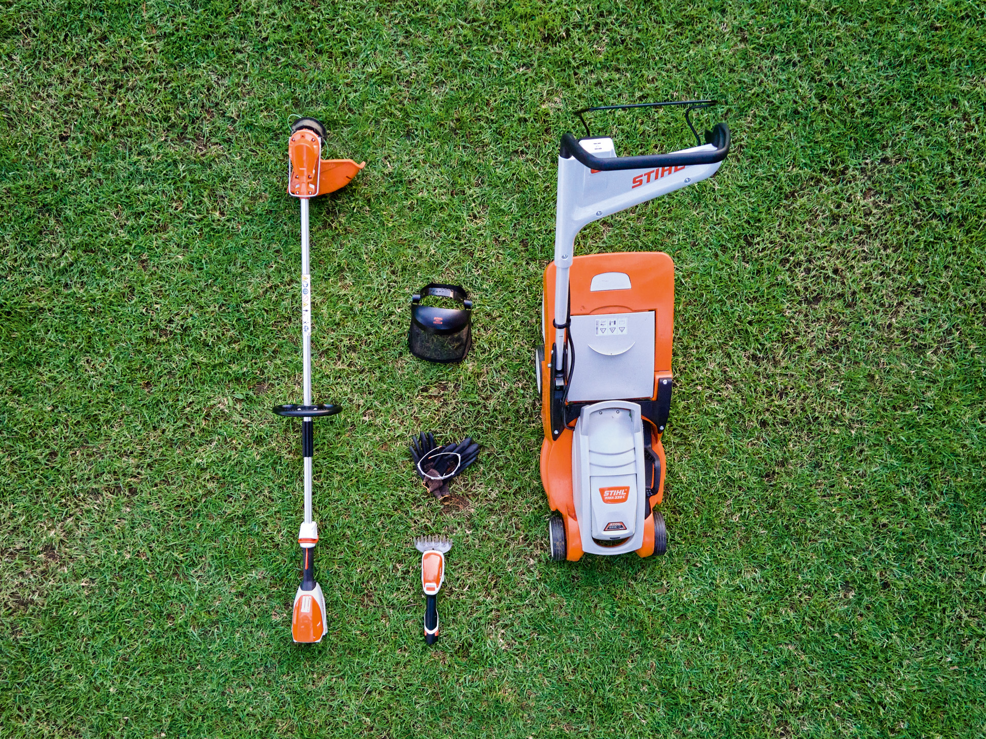 STIHL Rasenmäher, Motorsense und Akku-Strauchschere HSA 26 liegen auf einem Rasen