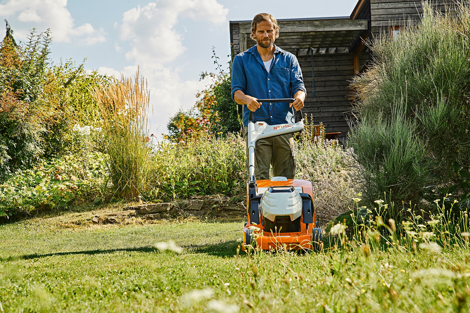 Mann betreibt mit STIHL Akku-Rasenmäher RMA 448 P-C auf einem bewachsenen Grundstück Rasenpflege im Sommer