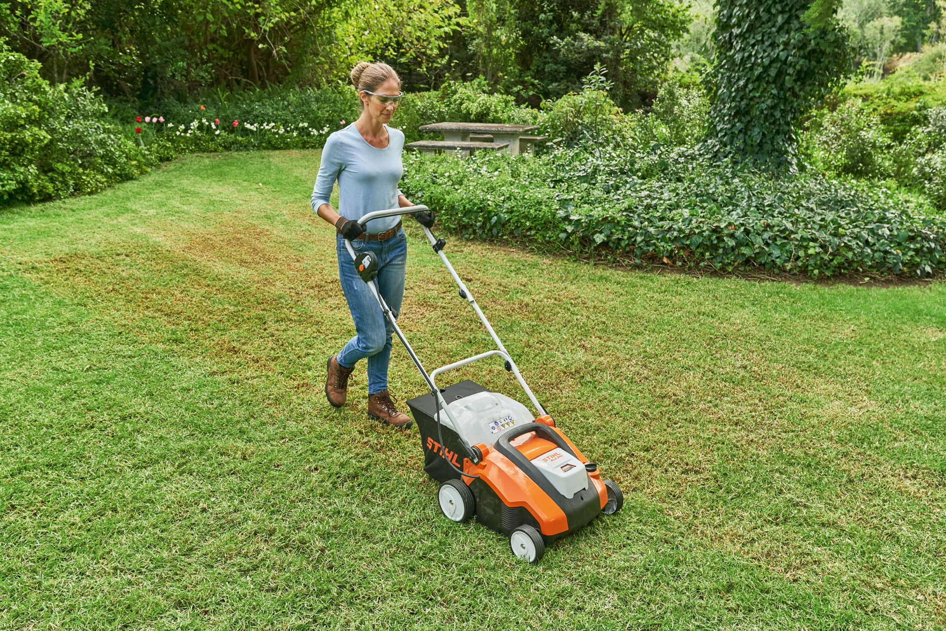 rau mit Schutzbrille und Arbeitshandschuhen vertikutiert kleine Rasenfläche mit STIHL Akku-Rasenlüfter RLA 240.