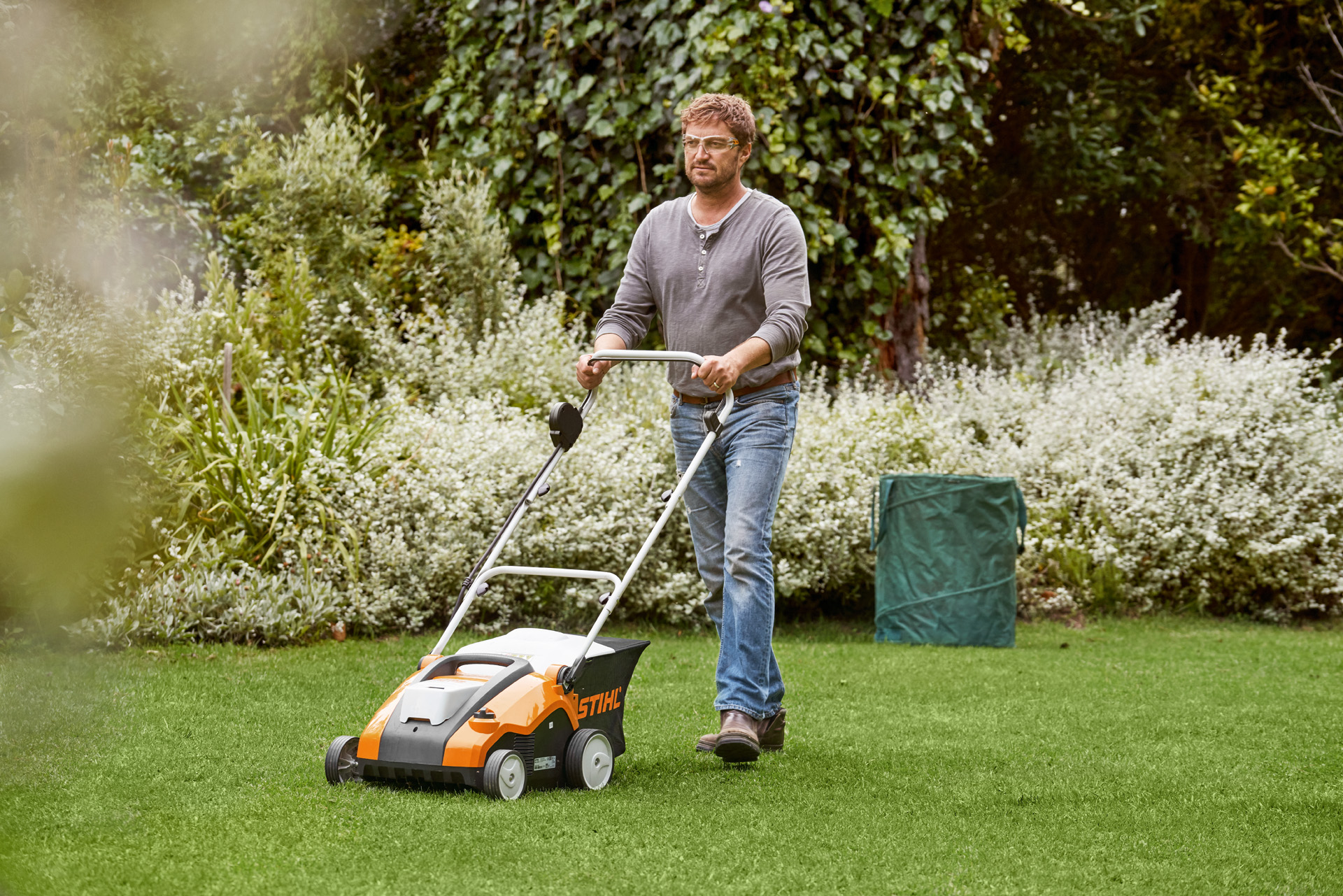 Mann vertikutiert grünen Rasen mit einem STIHL Akku-Rasenlüfter RLA 240