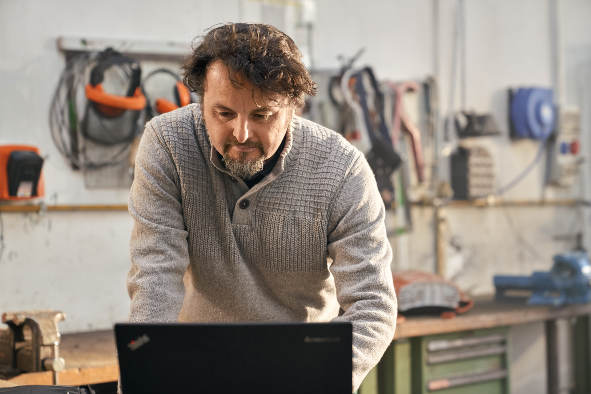 Mann vor einem Laptop in einer Werkstatt mit STIHL Geräten und Werkzeugen 