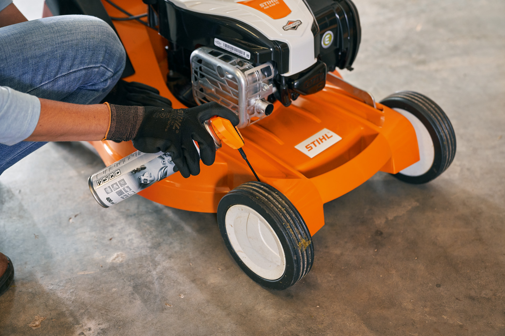 Frau lagert Ihren STIHL Benzin-Rasenmäher RM 448 TC in einer Garage 