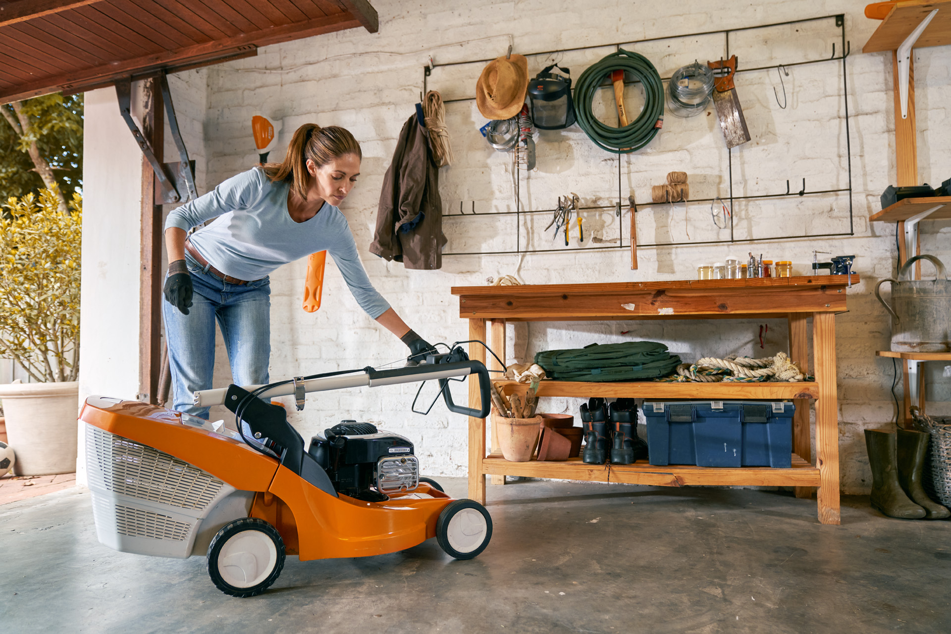 Frau macht den STIHL Benzin-Rasenmäher RM 448 TC in der Garage winterfest und lagert ihn