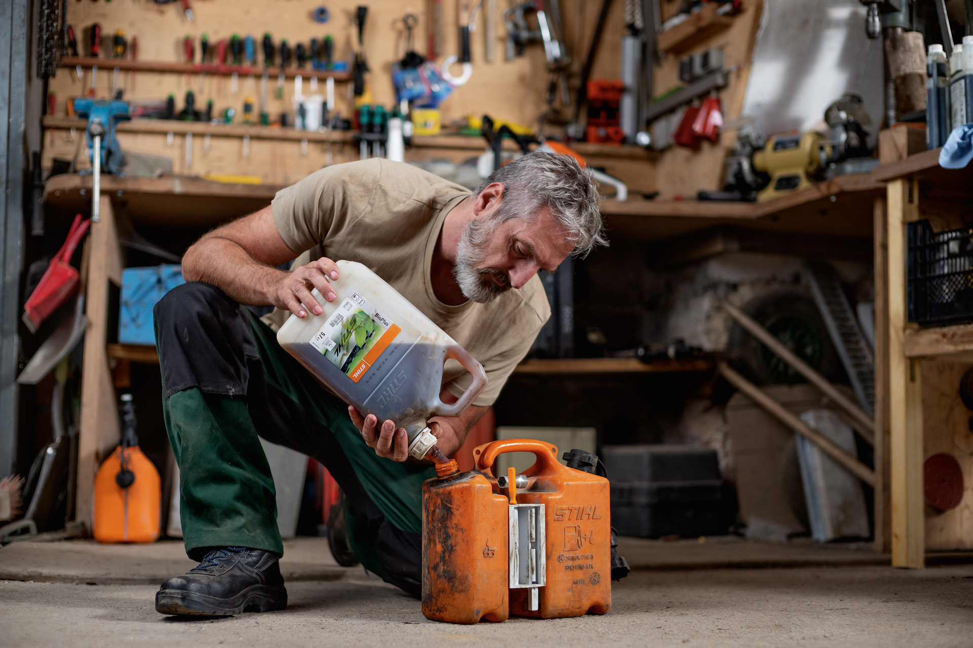 Mann kniet auf Werkstattboden und füllt STIHL Kraftstoff in einen orangenen Kanister