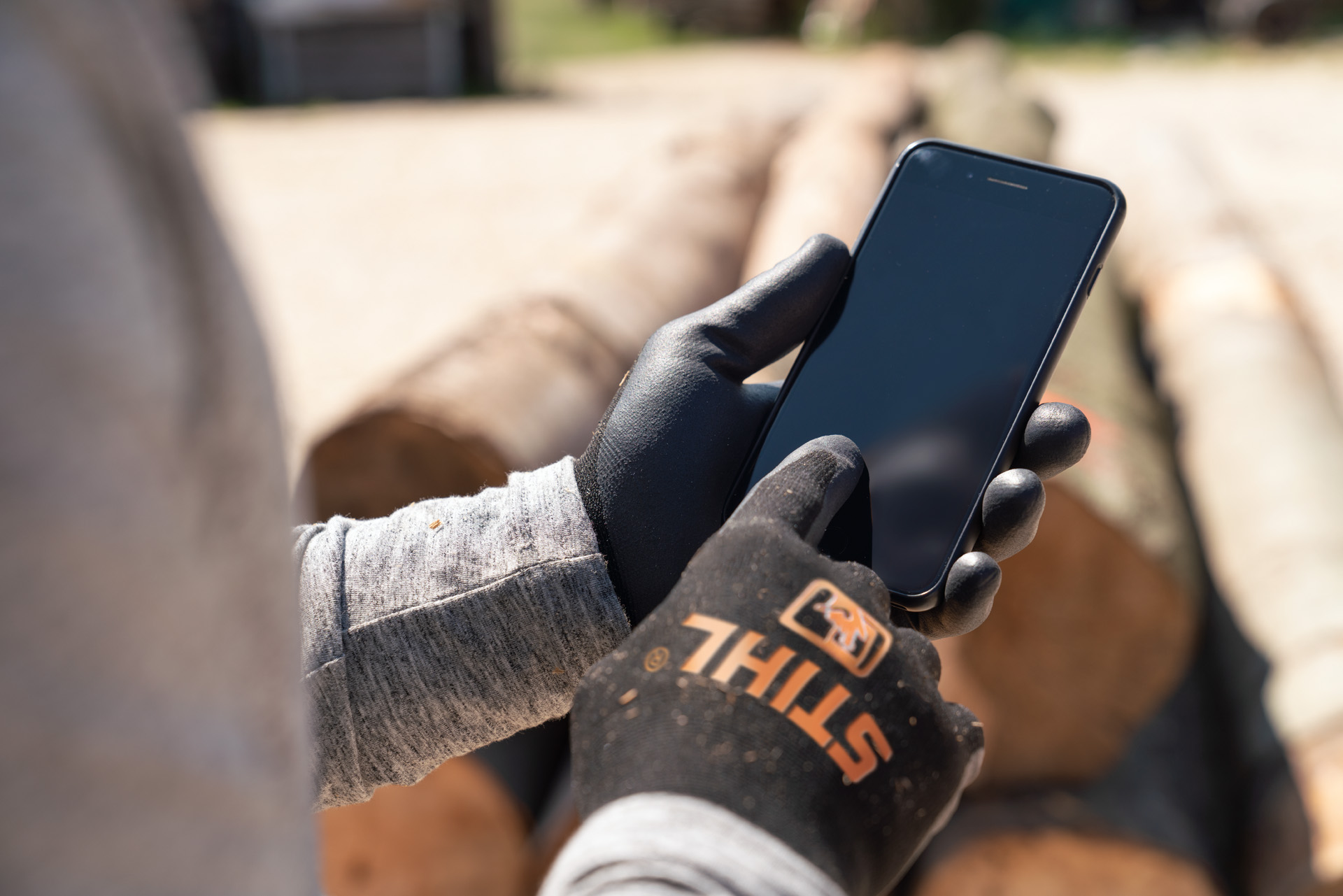Ein Mann mit STIHL Schutzhandschuhen tippt auf seinem Smartphone.