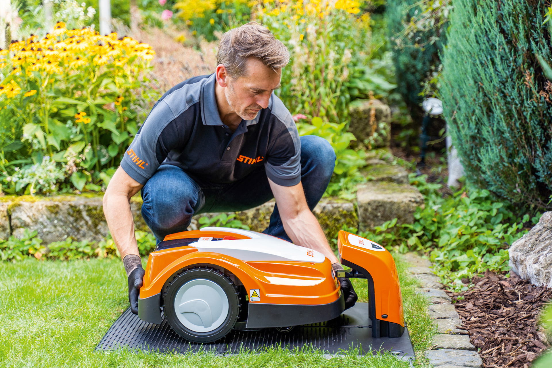 STIHL Fachhändler stellt einen STIHL iMOW Mähroboter in seine Ladestation in einem Garten