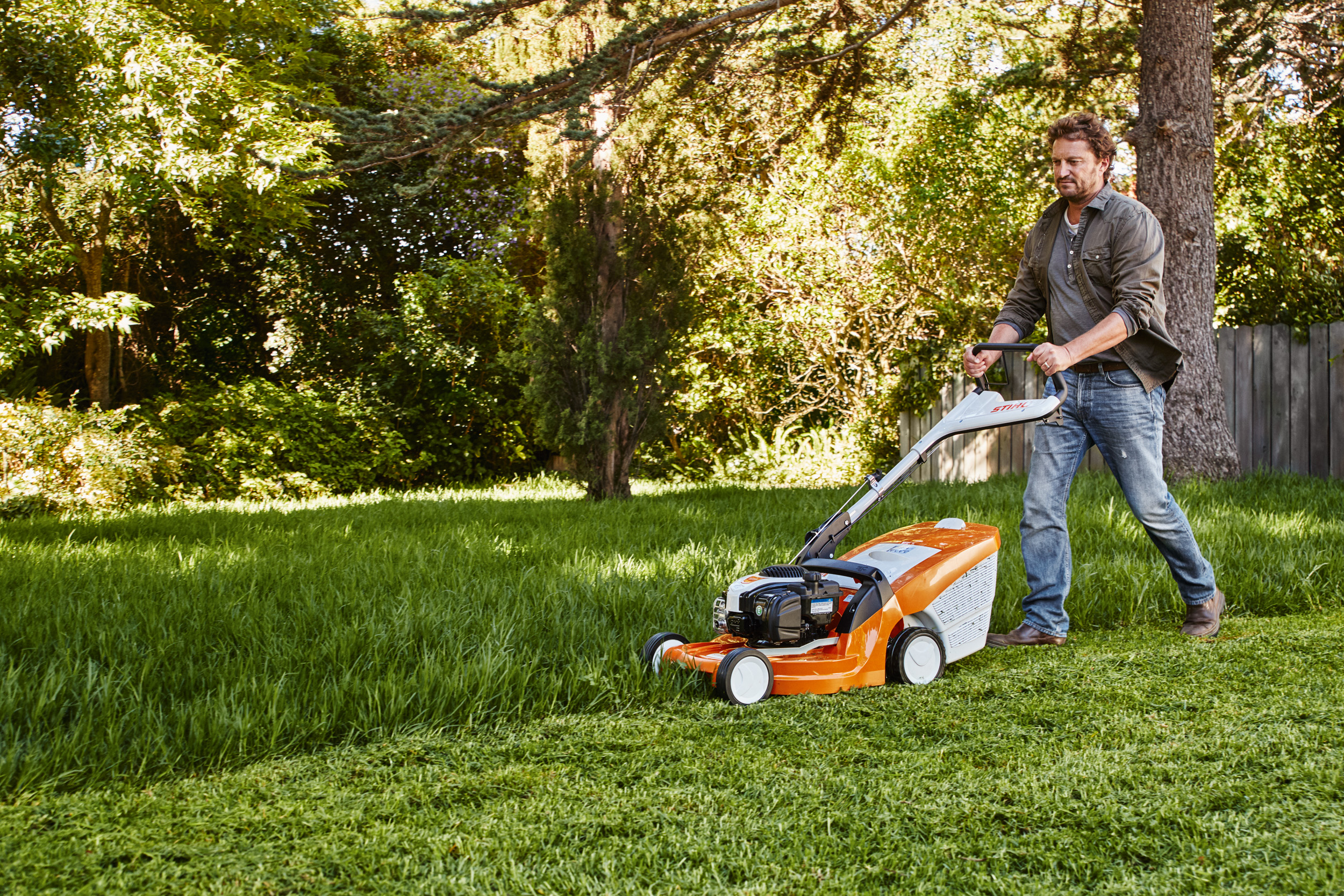 Ein Mann mäht in einem Garten den Rasen mit einem STIHL Rasenmäher 