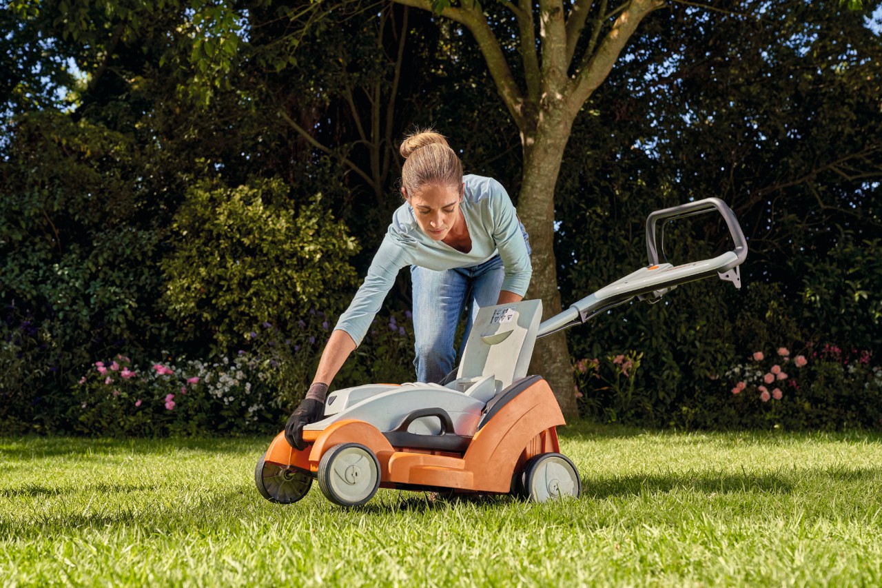 Eine Frau beugt sich nach unten, um den STIHL RMA 339 C wieder an seinen Platz zu stellen.