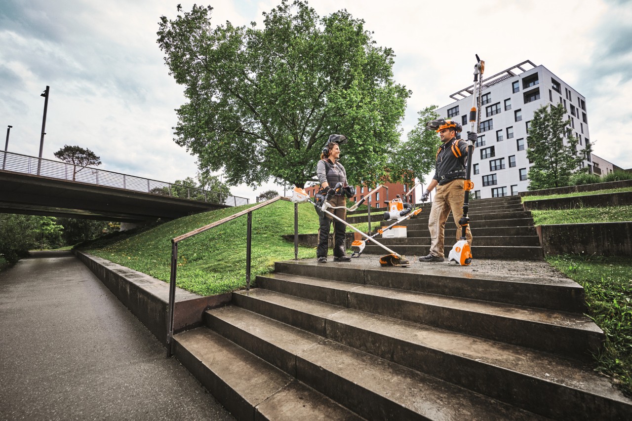 Zwei Personen mit verschiedenen Geräten aus dem ALLPRO-Akkusystem stehen auf einer Treppe vor Gebaäuden.
