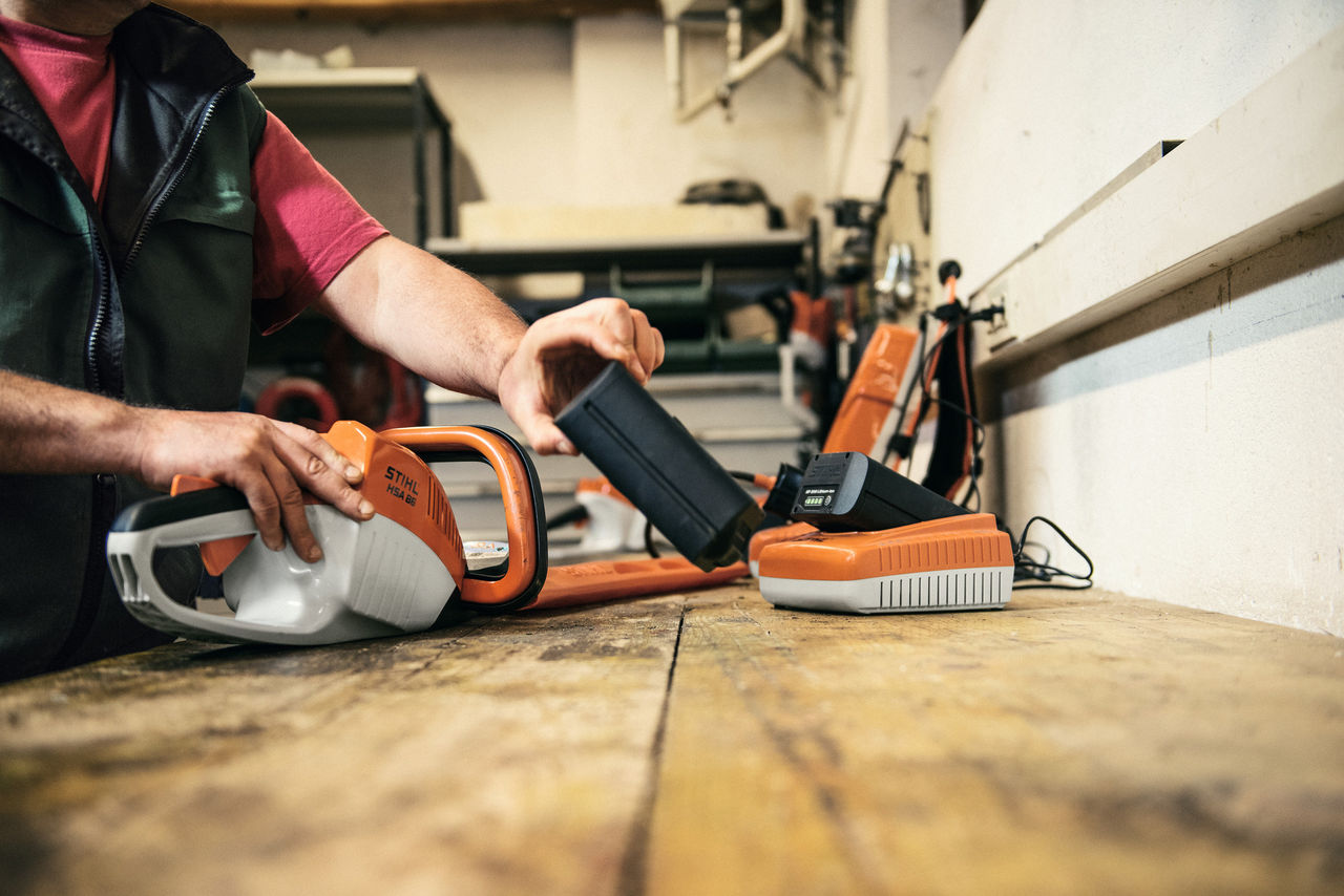 Mann beim Wechseln des STIHL AP-Akkus der Akku-Heckenschere STIHL HSA 86, ein STIHL AP-Akku im Ladegerät