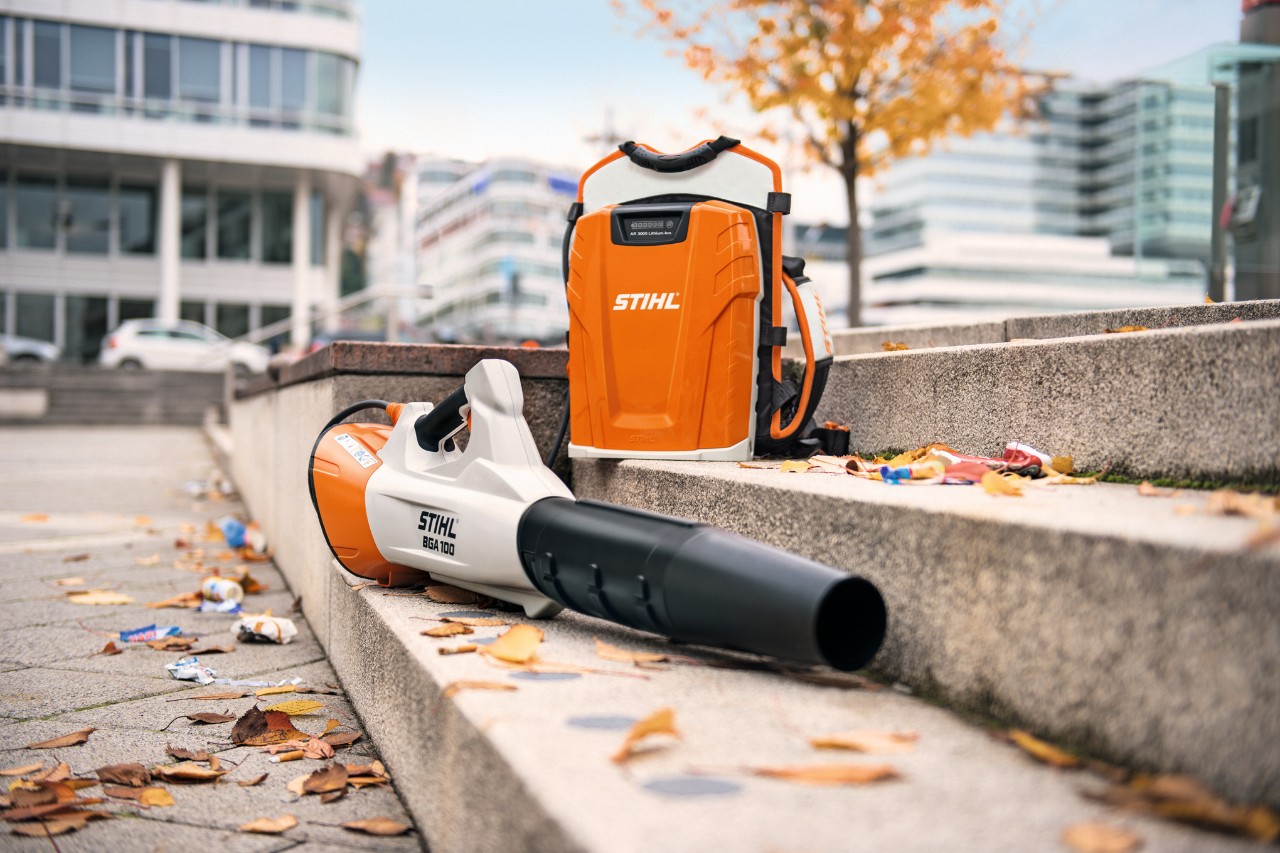 Auf einer Steintreppe mit einigen Laubblättern liegen der Akku-Laubbläser STIHL BGA 100 und der rückentragbare Profi-Akku STIHL AR 3000 L