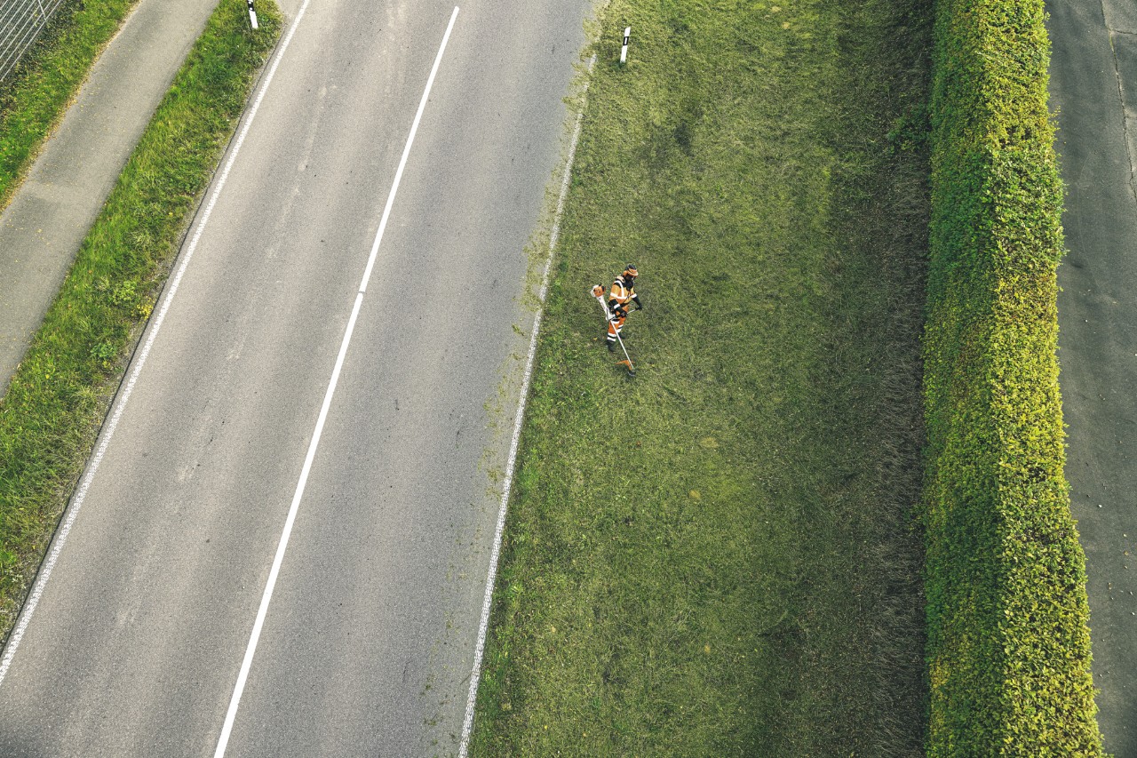 Professioneller Landschaftsgärtner mäht Gras an einer Schnellstraße