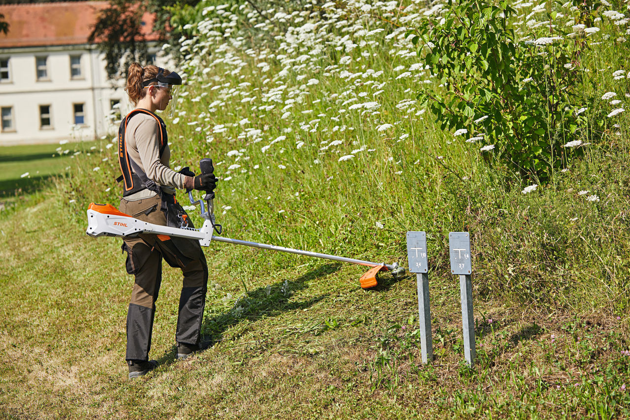 Frau mäht Gras mit dem kabellosen Freischneider STIHL FSA 135 für Profis, Standortansicht.