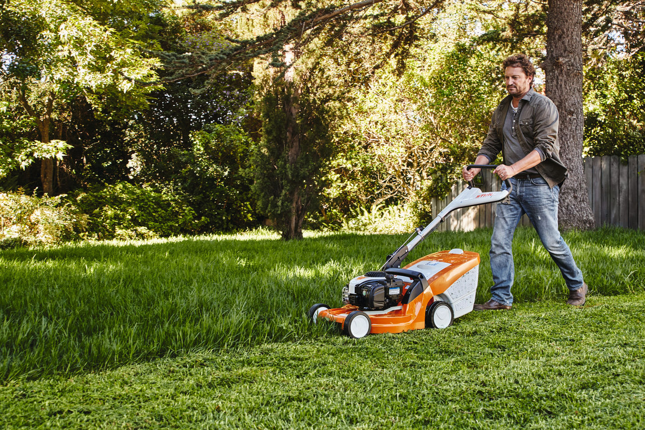 Ein Mann mäht in einem Garten den Rasen mit einem STIHL Rasenmäher 