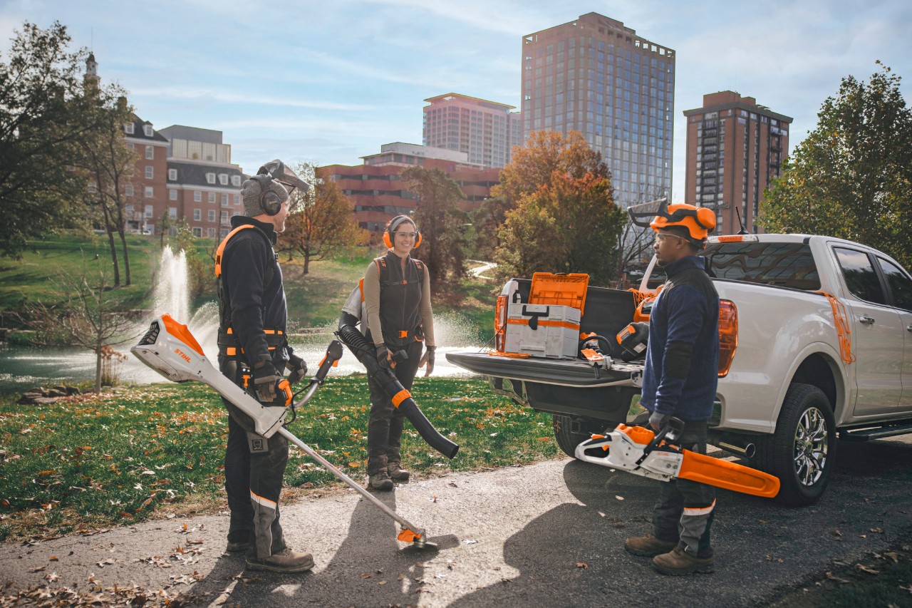 Gruppe professioneller Landschaftsgärtner, die um ihre Fahrzeuge herumstehen und sich mit STIHL-Akkuwerkzeugen auf ihre Arbeit vorbereiten.